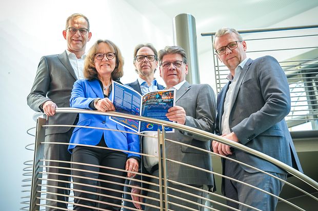 Gruppe von f&uuml;nf Personen auf einer Treppe mit den Umfrageergebnissen als Brosch&uuml;re in der Hand