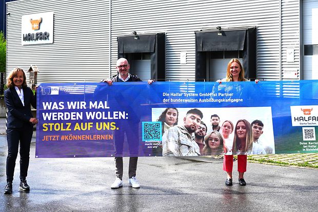 Vier Personen stehen vor dem Geb&auml;ude der Firma Halfar und halten ein gro&szlig;es Banner zur IHK-Ausbildungskampagne.