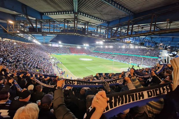 Fu&szlig;ballstadion bei Abendspiel, vollbesetzte R&auml;nge, Fans halten Arminia-Bielefeld-Schals hoch.