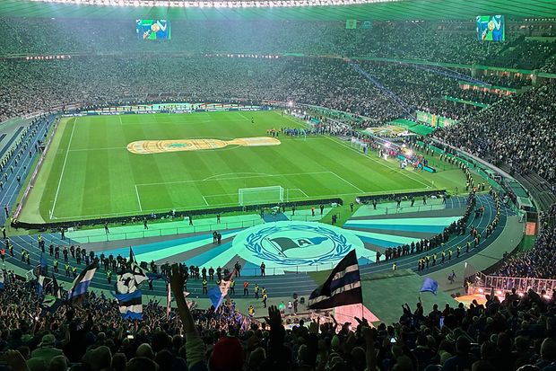 Abendstimmung im vollen Fu&szlig;ballstadion mit Choreografie und Arminia-Bielefeld-Fans im Vordergrund.