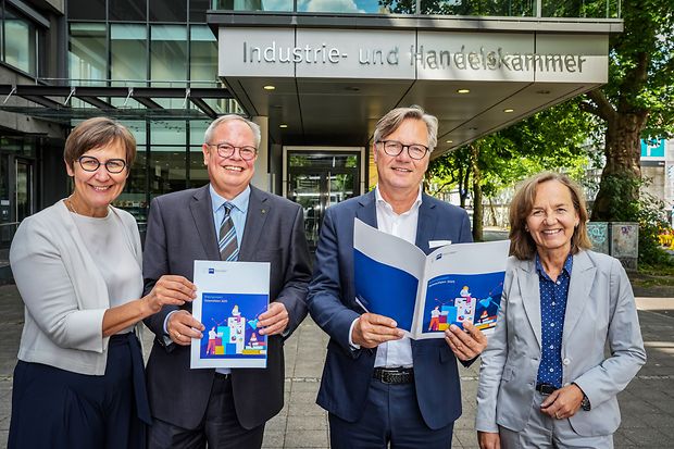Vier Personen stehen l&auml;chelnd vor der Industrie- und Handelskammer und pr&auml;sentieren eine Brosch&uuml;re zum Bildungsreport 2025