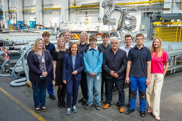 Gruppenfoto in Industriehalle mit "275"-Ballons im Hintergrund.