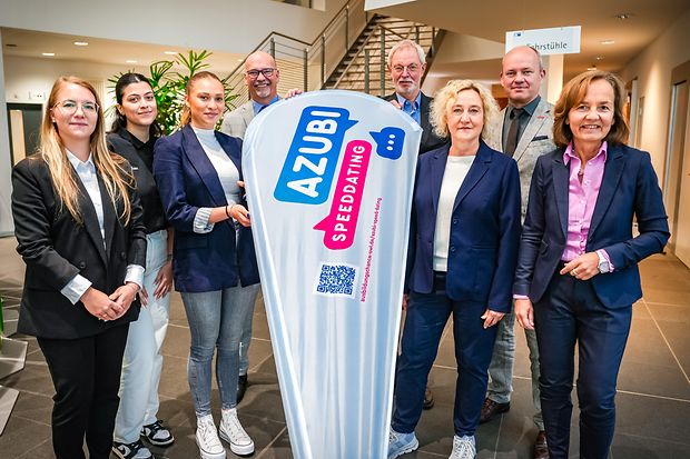 Gruppe vor Azubi-Speed-Dating-Werbebanner in Innenraum.