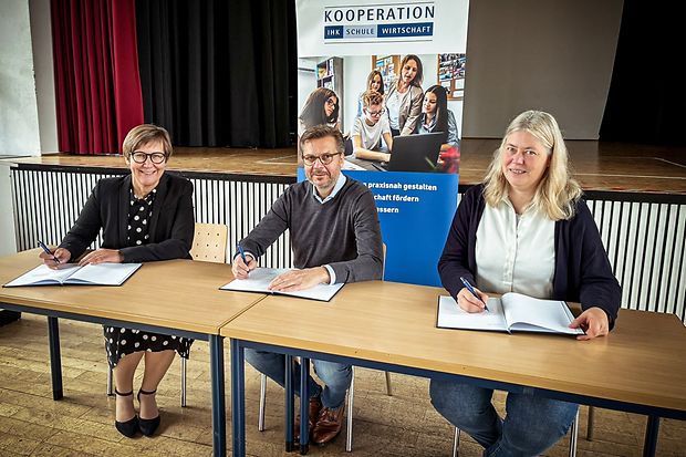 Drei Personen unterzeichnen eine IHK-Schulkooperation