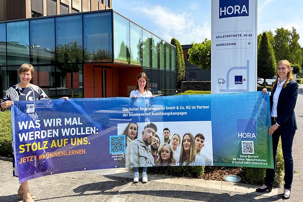 Drei Frauen pr&auml;sentieren ein Banner zur IHK-Ausbildungskampagne vor dem Firmengeb&auml;ude der HORA in Schlo&szlig; Holte-Stukenbrock