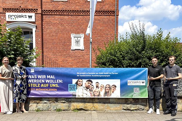 Vier Personen pr&auml;sentieren ein IHK-Ausbildungsbanner vor dem Geb&auml;ude der projekt w Systeme aus Stahl GmbH in Schlo&szlig; Holte.