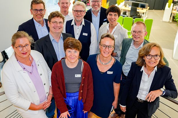 Gruppenfoto von zw&ouml;lf Personen auf einer Treppe in einem modernen B&uuml;rogeb&auml;ude.