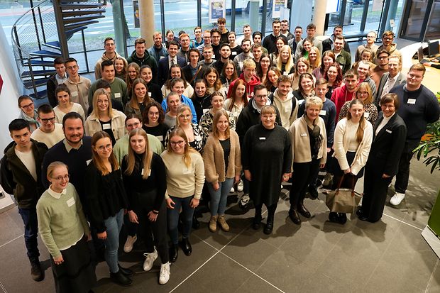 Gro&szlig;e Gruppe junger Menschen posiert l&auml;chelnd in einem modernen Foyer f&uuml;r ein Gruppenfoto.