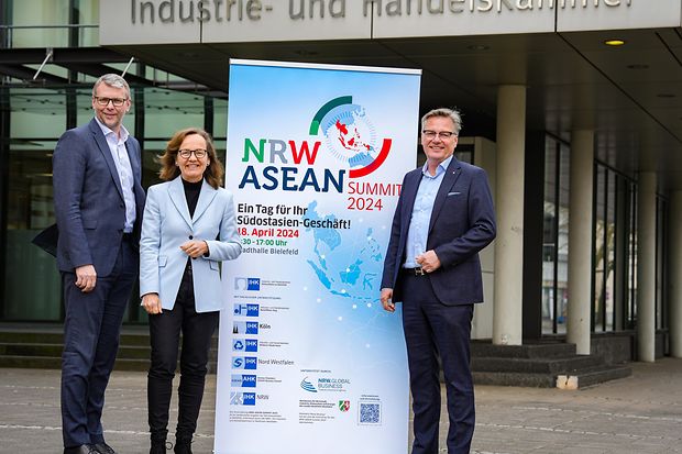 Drei Personen stehen vor der IHK neben einem Roll-up f&uuml;r den NRW-ASEAN Summit 2024 &ndash; Fokus auf internationale Wirtschaft.