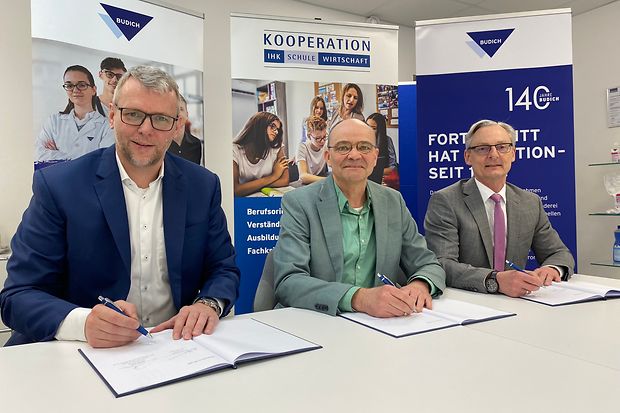 Drei M&auml;nner im Anzug sitzen an einem Tisch und unterzeichnen eine Kooperation zwischen IHK, Schule und Unternehmen &ndash;