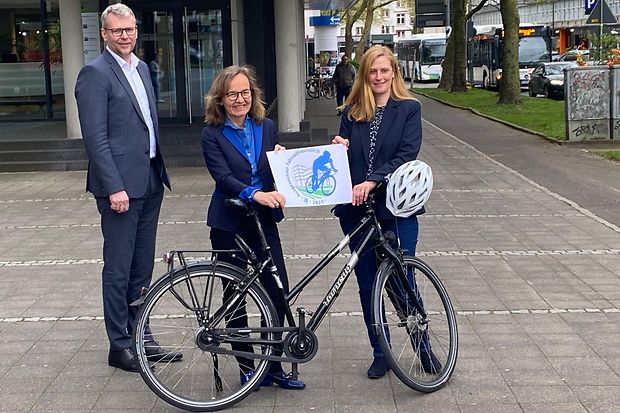 Drei Personen stehen mit Fahrrad vor der IHK, halten ein Schild zur Aktion &bdquo;Fahrradfreundlicher Arbeitgeber 2024&ldquo;.