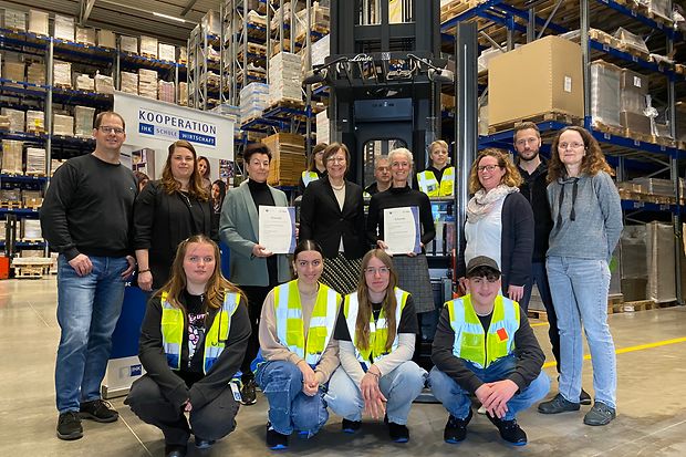 Gruppenfoto in einem Logistiklager mit Gabelstapler &ndash; &Uuml;bergabe von IHK-Urkunden im Rahmen einer Schulkooperation