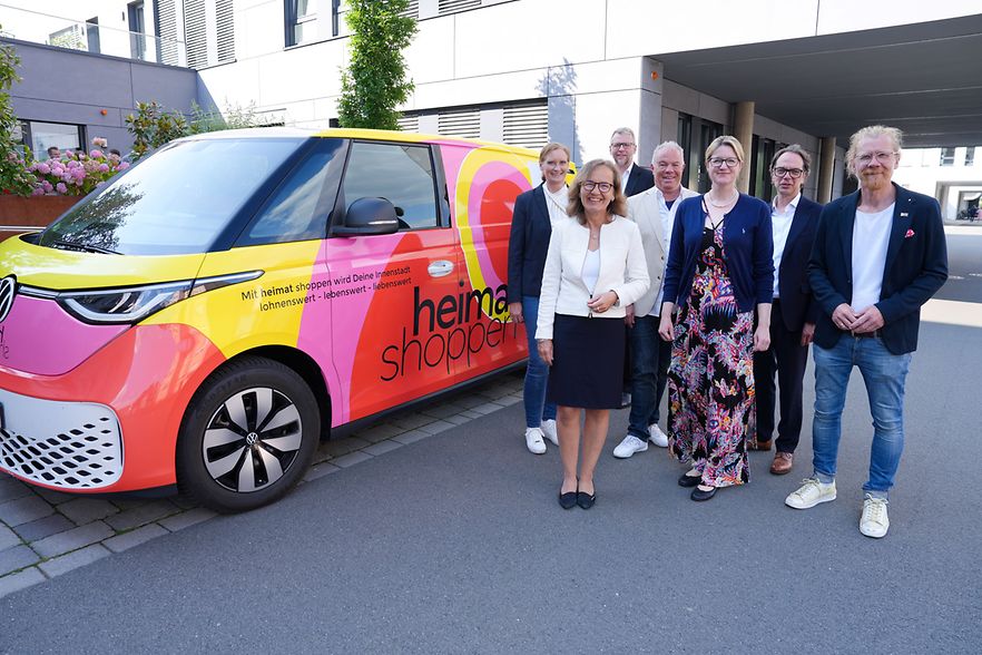 Sieben Personen stehen neben einem &bdquo;heimat shoppen&ldquo;-Auto in der Innenstadt 
