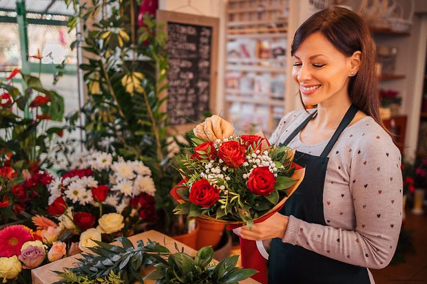 Symbolbild: Eine Floristin arrangiert einen Strau&szlig; roter Rosen