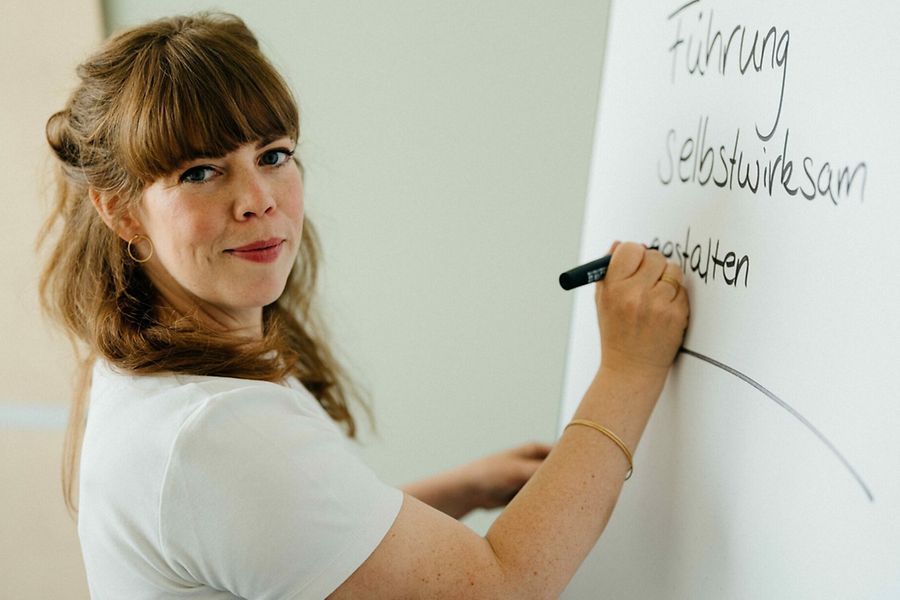 Frau schreibt an Whiteboard mit Text ‚Führung selbstwirksam gestalten'