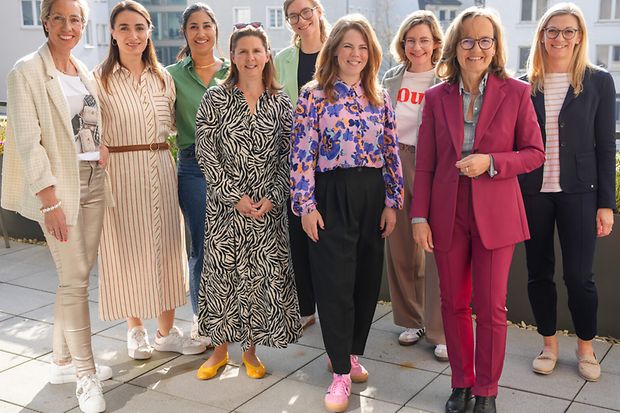 Neun Frauen stehen l&auml;chelnd auf Terrasse bei Sonnenschein