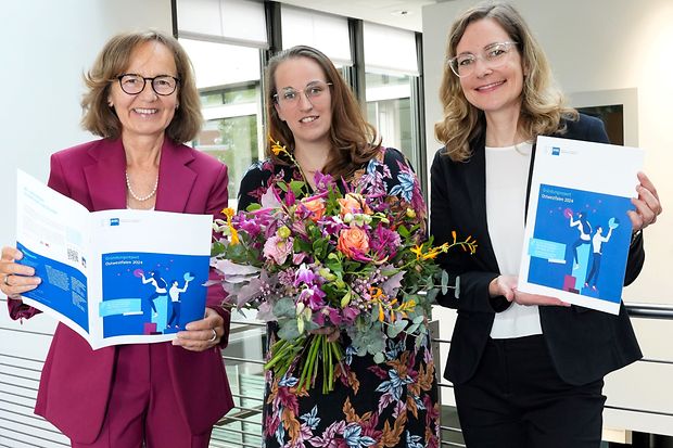 Drei Frauen mit Blumen und Report: Frauen halten den Gr&uuml;ndungsreport Ostwestfalen 2024, eine mit Blumenstrau&szlig;.