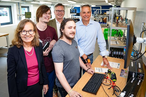 Unternehmensbesuch mit jungen Besch&auml;ftigten an einem technischen Arbeitsplatz.