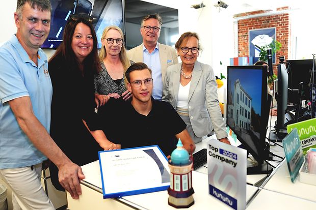Teamfoto im B&uuml;ro mit Auszeichnung: Mitarbeitende eines Unternehmens mit IHK-Urkunde und kununu-Auszeichnung.