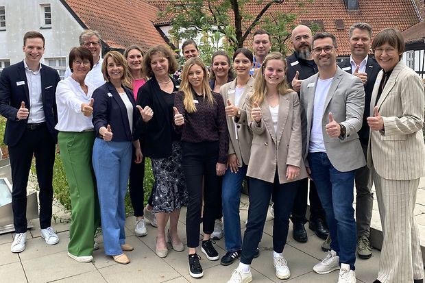 Eine Gruppe von Frauen und M&auml;nnern steht drau&szlig;en beisammen und zeigt Daumen hoch.