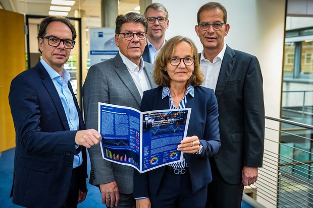Gruppe von f&uuml;nf Personen pr&auml;sentiert ein Magazin mit Grafiken und Diagrammen.