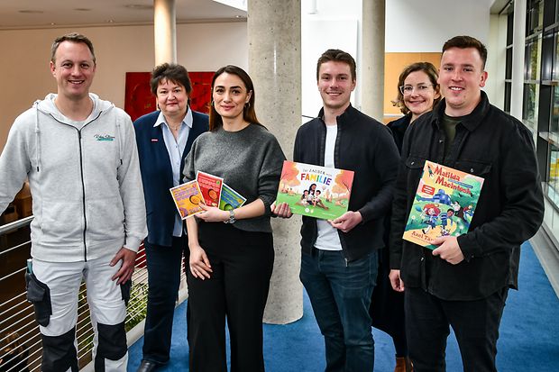 Gr&uuml;nderinnen und Gr&uuml;nder mit Gr&uuml;ndungsberatern; zwei halten Kinderb&uuml;cher, eine Werbemittel.