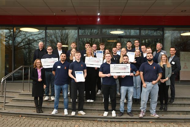 Gruppenfoto mit IHK-Vertretern und den teilnehmenden Auszubildenden. Einige halten Schecks in der Hand.