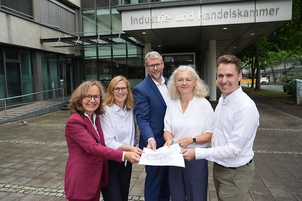 F&uuml;nf Personen vor der IHK halten gemeinsam eine Karte und l&auml;cheln in die Kamera.