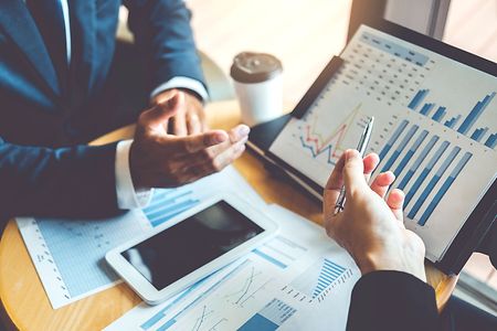 Zwei Personen besprechen Diagramme und Finanzdaten an Tisch mit Tablet