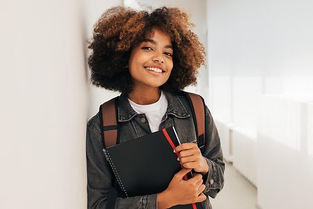 Portr&auml;t einer Studentin, die an einer Wand lehnt und in die Kamera blickt