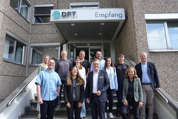 Gruppenfoto vor dem Empfangsbereich der Firma DFT mit Mitarbeitenden und Besuchenden