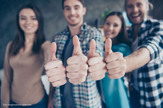 Vier junge Menschen zeigen l&auml;chelnd den Daumen nach oben &ndash; Zeichen f&uuml;r Zustimmung und Motivation.