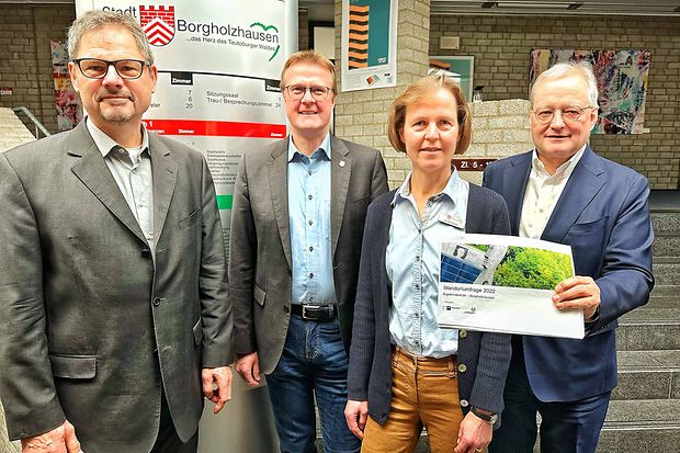 Vier Personen stehen im Foyer des Rathauses Borgholzhausen. Eine Frau h&auml;lt einen Bericht zur Standortumfrage 2022 in den H&auml;nden