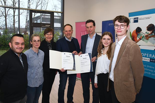 Sieben Personen, darunter zwei Jugendliche, pr&auml;sentieren gemeinsam zwei Urkunden.