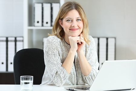 l&auml;chelnde Mitarbeiterin an ihrem Schreibtisch