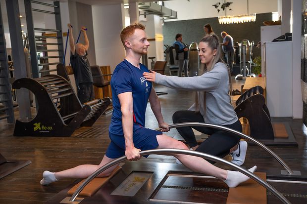 Junger Mann trainiert im Fitnessstudio unter Anleitung einer Trainerin