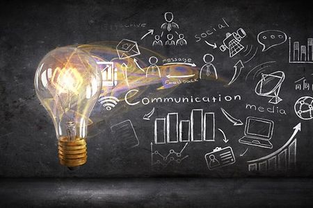 Leuchtende Gl&uuml;hbirne vor Wand mit gezeichneten Symbolen und dem Wort &bdquo;Communication&ldquo;