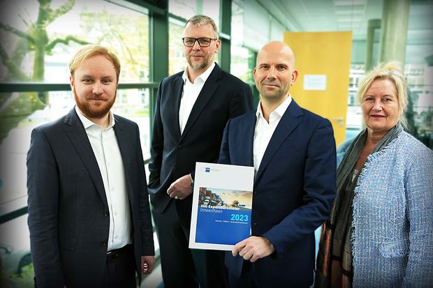 Vier Personen in Businesskleidung pr&auml;sentieren ein Dokument mit der Aufschrift &bdquo;IHK-Exportbarometer Ostwestfalen 2023&ldquo;.