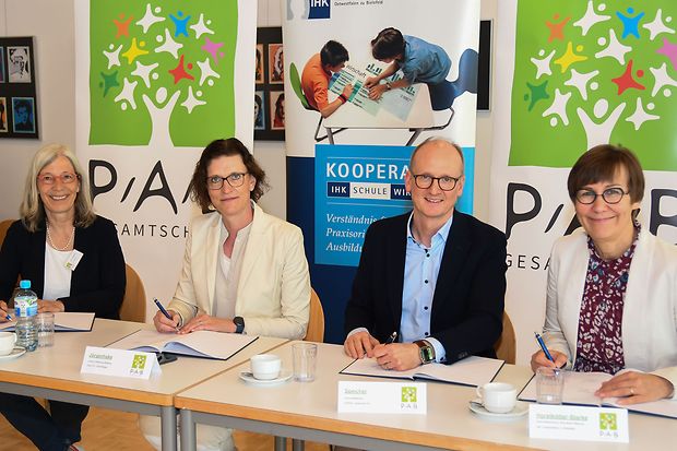 Vier Personen sitzen an einem Tisch und unterzeichnen eine Kooperationsvereinbarung zwischen Schule und IHK.