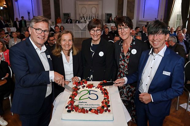 F&uuml;nf Personen schneiden gemeinsam eine gro&szlig;e Torte zum 25-j&auml;hrigen Jubil&auml;um der IHK Akademie Ostwestfalen an.