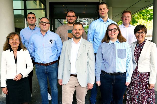 Neun Personen, darunter Absolventen, stehen vor einem Geb&auml;ude der IHK in Bielefeld.