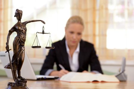 Anw&auml;ltin am Schreibtisch mit Justitia-Figur im Vordergrund