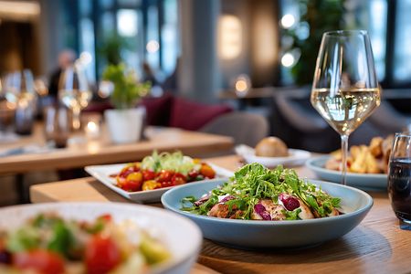 Tisch im Restaurant mit Salat, Beilagen und gef&uuml;llten Weingl&auml;sern.