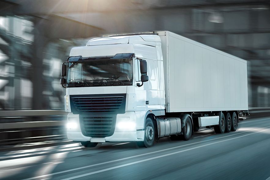Wei&szlig;er Lkw f&auml;hrt auf einer Stra&szlig;e mit eingeschaltetem Licht.