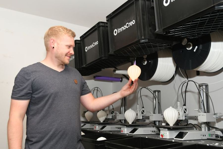 Mann betrachtet ein Objekt aus einem 3D-Drucker.