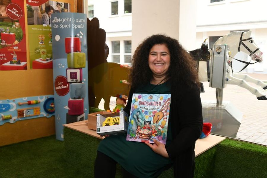 Frau in Spielecke mit Kinderbuch „Dinosaurier“ und Spielzeug.