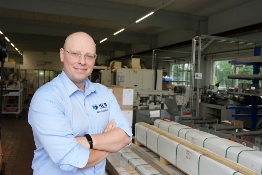 Mann in Arbeitskleidung steht lächelnd in Produktionshalle.