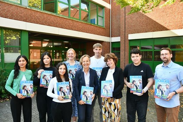 Sch&uuml;ler und Erwachsene pr&auml;sentieren Ausbildungsatlas vor Schule.