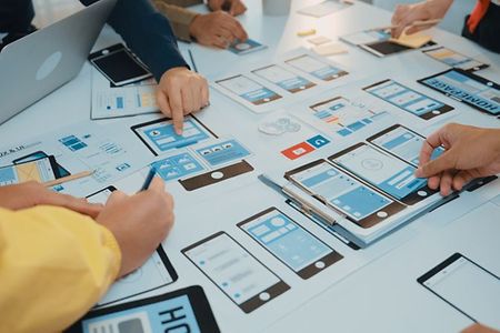 Team arbeitet an App-Design und Wireframes auf gro&szlig;em Tisch.