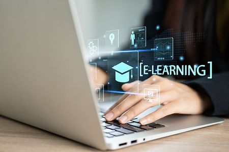 H&auml;nde tippen auf Laptop mit Schriftzug &bdquo;E-Learning&ldquo;.